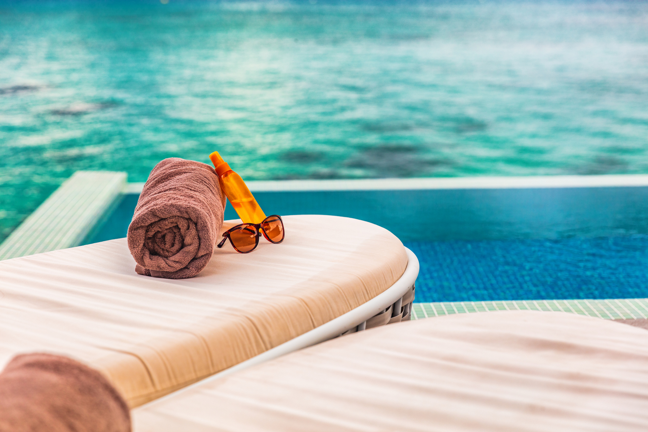 Hotel infinity swimming pool background sun loungers background for luxury relaxing holidays in Caribbean destination. Tropics lifestyle sunblock and sunglasses solar protection.